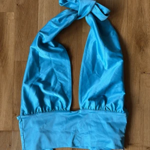 Turkos omlott halterneck topp - Snygg turkos halterneck topp med bred knytning i nacken och omlottkänsla. Toppens material har en lätt glans och känns mjukt mot huden, perfekt för att sticka ut. Bred resår nedtill för extra stöd och cool look💙🩵