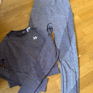 Grå långärmad träningströja och tights  157 - Superskön grå långärmad träningströja och tights från 157. Tröjan är sömlös med ribbade detaljer på ärmar och sidor, och har en tight passform som sitter snyggt på kroppen. Perfekt för gymmet eller löprundan. Materialet är stretchigt och andas bra. 120kr för hela settet. 