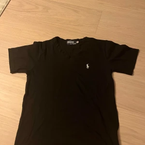 Svart t-shirt från Polo Ralph Lauren - Svart t-shirt från Polo Ralph Lauren i 100% bomull. Klassisk v-ringning och korta ärmar, med den ikoniska broderade loggan på bröstet. Enkel och stilren modell som passar perfekt till jeans eller shorts. priset kan sänkas