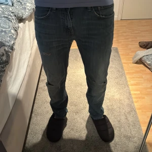 Levi's jeans - Säljer ett par klassiska Levi's 511 jeans i blå tvätt med snygga slitningar på knäna och lätt urtvättad look. Jeansen har normal passform, fem fickor och är tillverkade i mjukt jeanstyg. Perfekta för dig som gillar en avslappnad men stilren vibe.