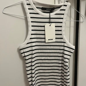 Randig ribbad linnetopp från Bik Bok - Säljer en fräsch vit och svart randig linnetopp från Bik Bok. Toppen är ribbad och ärmlös med klassisk rund halsringning. Perfekt för varma dagar och enkel att styla till jeans eller kjol. Superskön och stilren basic som passar till allt. Prislapp kvar