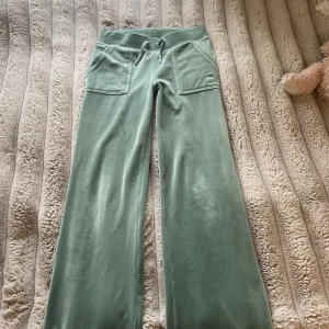 Gröna mjukisbyxor i velour - Mysiga ljusgröna mjukisbyxor i velour med bred resårmidja och snörning. Byxorna har stora fickor fram och bak, samt raka ben med relaxed fit. Perfekta för chill dagar och har en broderad logga på ena fickan framtill. Har ett ljust sträck längst ner 