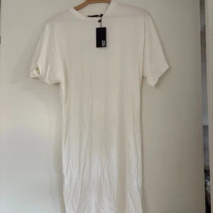 Vit t-shirtklänning stl S - Enkel och stilren vit t-shirtklänning i storlek S. Klänningen har rund halsringning, korta ärmar och rak passform. Tillverkad i mjuk bomull som känns skön mot huden. Perfekt för en avslappnad look. Transparent 