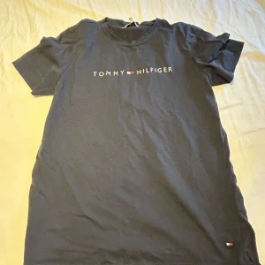 Svart t-shirt från Tommy Hilfiger - Svart t-shirt från Tommy Hilfiger med klassisk logga tryckt på bröstet och liten flagga nertill. T-shirten har rund halsringning och korta ärmar. Tillverkad i mjuk bomull för en skön känsla och enkel stil.