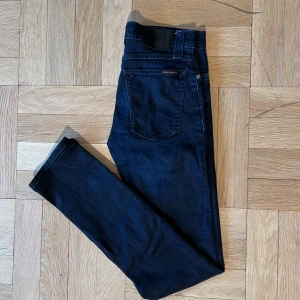 Mörkblå skinny jeans från Nudie - Snygga mörkblå jeans från Nudie Jeans med klassisk femficksdesign och diskret logga på bakfickan. Modellen är skinny fit med smala ben och låg till normal midja. Tillverkade i stretchig denim för en bekväm passform.
