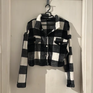 Svartvit rutig teddyjacka - Säljer en svartvit teddyjacka från Shein med stora rutor och mjukt, fluffigt material. Jackan är croppad, har långa ärmar, två bröstfickor med knappar och klassisk krage. Perfekt för dig som gillar statement-plagg med cozy vibe.