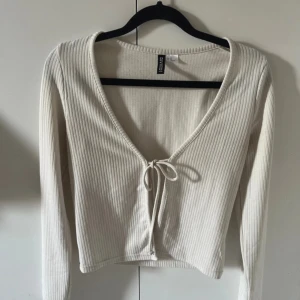 Ribbad vit omlottopp från H&M Divided - Säljer en ribbad vit omlottopp från H&M Divided i storlek XS. Toppen har lång ärm, v-ringning och knyt framtill. Den är croppad