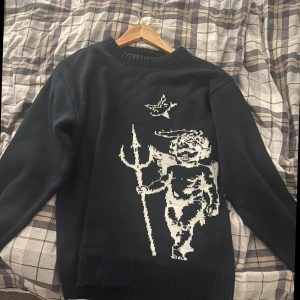 Mörk blå stickad tröja Laviago med ängel - Mörk blå tröja från Laviago med vit pixelgrafik av en ängel med treudd och fågel på framsidan. Baksidan har Laviago-logga i vitt. Tröjan har rund hals och långa ärmar, perfekt för dig som gillar unika motiv och streetwear-vibe. Den är i färgen Mörkblå.