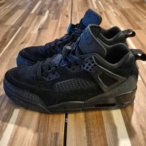 Svarta Nike Jordan 4 sneakers - Säljer ett par helsvarta Nike Jordan 4 sneakers med snygga detaljer och meshpaneler på sidorna. Skorna har snörning, robust sula och coola Brooklyn-loggor på hälen. Ovandelen är i mocka och syntet, perfekt för dig som gillar streetstyle.