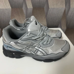 Grå Asics GEL sneakers med svarta sulor - Snygga Asics GEL sneakers i olika grå nyanser med silvriga detaljer och svart sula. Skorna har mesh och syntetmaterial, klassisk snörning och sportig vibe. Perfekta för dig som gillar streetstyle och bekväma skor med cool design.