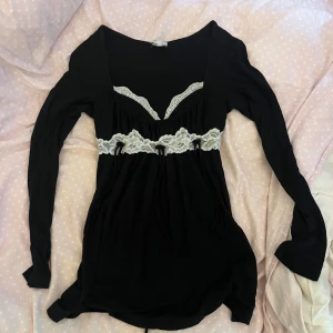 Svart babydoll tröja med spetsdetaljer - Säljer en svart tröja med lång ärm och vit spets vid byst och midja. tröjan har en djup v-ringning och fina knytband under spetsen. Mjuk och skön, perfekt för dig som gillar romantiska detaljer och kontraster.