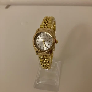 Guldfärgad klocka från Yolako - Stilren guldfärgad klocka från Yolako med länkarmband och rund urtavla i silver. Urtavlan har glittriga stenar som timmarkeringar och klassiska visare. Perfekt accessoar för att lyfta din outfit.