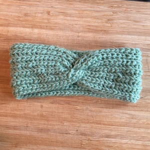 Virkat grönt pannband twistad front - Mysigt virkat pannband i ljusgrön färg med twistad front. Perfekt för att hålla öronen varma under kyliga dagar. Tjockt garn och bred modell ger en skön känsla och snygg look. Passar dig som gillar enkel men trendig stil. Mått på 24 cm x 10 cm