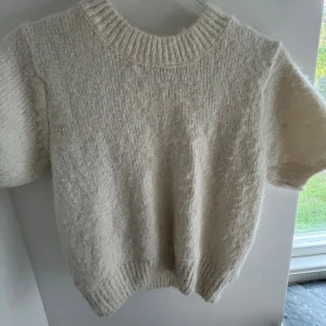 Vit stickad kortärmad tröja Gina Tricot - Mysig vit stickad tröja från Gina Tricot med korta ärmar och ribbad kant vid hals, ärmslut och nederkant. Perfekt för lager-på-lager och har en enkel, clean look som funkar till allt. Materialet känns fluffigt och mjukt.