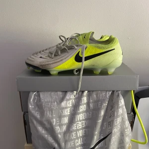 Nike fotbollsskor gul/vit strl 44 - Säljer ett par Nike fotbollsskor i storlek 44. Modellen är Nike phantome NIKE PHANTOM GX II ELITE FG MAD VOLTAGE - SILVER/SVART/NEON ny pris för 3000 så mitt pris är på 1500 pga användning men annars inga andra problem.