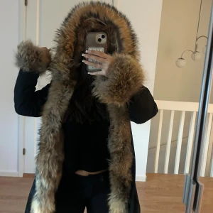 Svart parkas med päls Dolly - Säljer en svart parkas ( Dolly) med oversized huva och breda muddar i fluffig brun päls. Jackan är perfekt för kalla dagar när du vill sticka ut. Pälsen går längs hela öppningen och runt huvan för en riktigt maffig look. Jackan har aldrig använts tidigare då den är för stor, den är storlek S men passar även M. Alla pälsdetaljer är avtagbara. Fickor på sidorna och det går ett snöre runt midjan som man kan dra åt. Jackan är beställd från ssshop. Nypris:3999kr Säljs:2500 kr pris går att diskuteras!