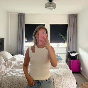 Vit ribbad linnetopp med cut out - Säljer en vit ribbad linnetopp med cool cut out-detalj vid axeln. Toppen är ärmlös och har en tight passform som sitter snyggt mot kroppen. Perfekt att styla med jeans eller kjol för en trendig look.