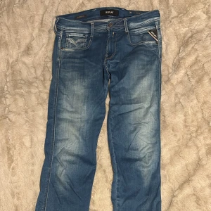 Replay Anbass Hyperflex jeans blå - Snygga blå Replay Anbass Hyperflex jeans med coola slitningar. Jeansen har raka ben, normal/skinny passform och är tillverkade i stretchigt denim för extra komfort. Perfekta för dig som vill ha stilrena och bekväma jeans med stilig kändla.