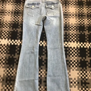 True Religion ljusblå bootcut jeans - Säljer ett par ljusblå jeans från True Religion med bootcut passform. Jeansen har klassiska fickor bak med lock och dekorativa sömmar samt silverfärgade. Storlek 26 och modellen Becca som nya!!!🤭🤭