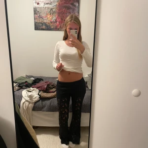 Svarta spetsbyxor med låg midja - Säljer ett par svarta byxor i genombruten spets med blommigt mönster. Byxorna har låg midja och utsvängda ben för en trendig look. Perfekta för dig som vill sticka ut och gillar en edgy stil.