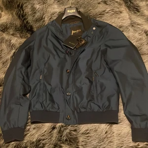 Mörkblå bomberjacka från MooRER - Säljer en mörkblå bomberjacka från MooRER med muddar och midja, dragkedja och knappar framtill samt två fickor med dragkedja på både inne och ute sida. Perfekt för dig som vill ha en clean och snygg jacka nu till hösten. Nypris på denna är 10 999kr. Jag köpte denna helt sprillans ny på Nk men köpet var inte tillräckligt planerat så nu är den för liten. Prislappen sitter kvar. Jag har även kvitto på jackan. Jackan är ganska svår att få tag på. Skriv vid funderingar. Pris kan diskuteras!!