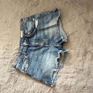 Blå jeansshorts Ariel mid waist - Säljer ett par blå jeansshorts från Wow Denim i modellen mid waist. Shortsen har slitna detaljer både fram och bak. Klassisk femficksmodell med bälteshällor och dragkedja. Perfekta för varma dagar och en avslappnad look.