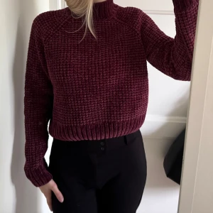 Vinröd stickad tröja med hög krage - Säljer en vinröd stickad tröja i storlek S med grov struktur och ribbade muddar. Tröjan har en hög krage och långa ärmar, perfekt för att hålla värmen. Materialet är mjukt och har en snygg, mörk vinröd ton. 