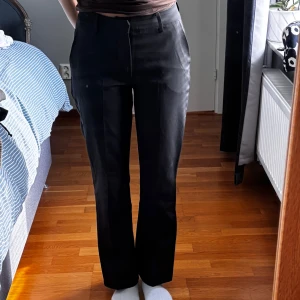 Svarta kostymbyxor med raka ben - Snygga svarta kostymbyxor med raka ben och pressveck. Byxorna har hällor för bälte, sidfickor fram och fuskfickor bak. De är midjehöga och har en klassisk, stilren look som passar till många olika outfits.