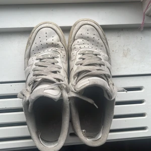 Nike Air Force 1 vita sneakers - Klassiska Nike Air Force 1 sneakers i vitt skinn med perforerad tå, snörning och rund tå. Snygg och tidlös modell med Nike-logga bak och på sulan. Perfekta för dig som gillar streetstyle och vill ha en ikonisk sneaker i garderoben.