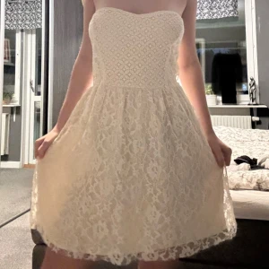 Spetsklänning Hollister - Supersöt axelbandslös kortklänning från Hollister i vit spets med hjärtformad överdel. Klänningen har smockad rygg för extra komfort och en lätt utställd kjol. Perfekt för sommarens alla tillfällen och ger en romantisk vibe. Det står storlek L på lappen men skulle vilja säga att M är mer realistiskt. Jag har normalt XS eller S, men den här var lite för stor därav säljer jag den.