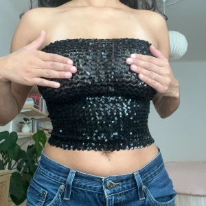 Svart paljett bandeau tubtopp - Svart tubtopp täckt av glittriga paljetter.🖤🖤🖤 Toppen är axelbandslös och har dragkedja i ryggen. Är stretchig och passar storlek XS-S, men passar bättre med mindre byst då den annars blir lite genomskinlig. 