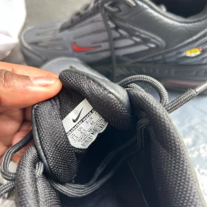 Nike Air Max Plus TN Svart/Röd - Säljer ett par Nike Air Max Plus TN i svart och grått med röda swoosh-detaljer och gula TN-loggor. Skorna har mesh- och syntetöverdel, snörning och en chunky sula med Tuned Air. Perfekta för dig som gillar streetwear och vill sticka ut med en ikonisk sneaker.