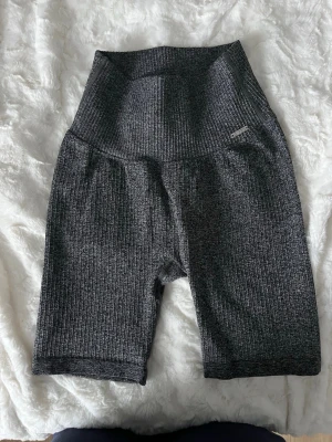 Mörkgrå ribbade shorts Aim'n - Säljer ett par mörkgrå ribbade cykelshorts från Aim'n med hög midja. Shortsen är stretchiga och har en tight passform, perfekta för träning eller chill. Materialet är mjukt och följsamt, och de har en diskret Aim'n-logga på sidan.