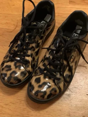 Leopard skor -  sneakers från Björn borg med glansigt leopardmönster i beige, svart och brunt. Skorna har svarta snören och en platt svart sula. Perfekta för dig som vill sticka ut med ett djurmönster och unik stil. Ge gärna prisförslag använda ca 3 ggr