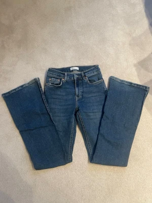 Gina tricot blå low bootcut jeans - Blåa Gina tricot jeans med bootcut passform och fem fickor. Jeansen har låg midja och är tillverkade i slitstarkt bomullsdenim. Perfekta för dig som gillar en tidlös och avslappnad look.