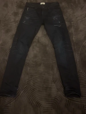 Mörkblå slim jeans från Jack and Jones R.D.D - Snygga mörkblå jeans från Jack and Jones i slim fit-modell. Jeansen har klassiska fem fickor, diskreta slitningar framtill och en patch i bakfickan som står R.D.D. Perfekta för dig som gillar en stilren och modern look. Storleken 31/32