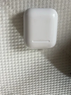 Vita trådlösa hörlurar AirPods - Säljer ett par vita trådlösa hörlurar från Apple, modell AirPods. Kommer med det klassiska kompakta laddningsetuiet i blank plast. Perfekta för musik, poddar och samtal på språng. Denna har ba en hörlurar där inne o e lite smutsig där inne
