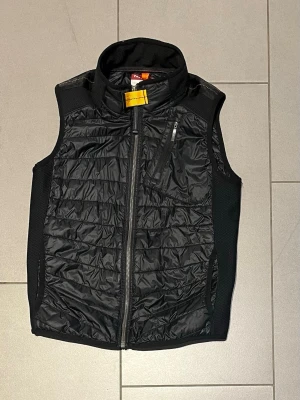 Svart dunväst från parajumers - Snygg svart dunväst från POC med quiltad framsida, hög krage och dragkedja hela vägen. Västen har en bröstficka med dragkedja och meshpaneler på sidorna för extra komfort. Perfekt för lager-på-lager och outdoor-looks.