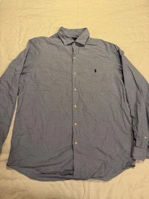 Blå skjorta från Polo Ralph Lauren - Klassisk blå skjorta från Polo Ralph Lauren med broderad logga på bröstet. Skjortan har lång ärm, knappar framtill och är tillverkad i mjuk bomull med stretch. Perfekt för en clean och stilren look.