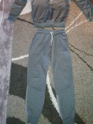 Grå sweatshirt från McKenzie och byxor - Sportig grå sweatshirt från McKenzie med svart tryck på bröstet där det står 'MCKENZIE ORIGINAL SPORTSWEAR'. Tröjan har rund halsringning och är tillverkad i ett mjukt, stretchigt material som passar perfekt till en avslappnad stil. Pris kan dras ner skriv med mig bara. Byxor ingår