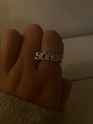 SÖDER ring i silver 925 - Cool ring i äkta silver med texten 'SÖDER' i stora bokstäver. Ringen är i massiv 925 sterling silver och har en modern, stilren design som sticker ut. Perfekt accessoar för dig som vill visa din kärlek till Södermalm eller bara gillar unika smycken.