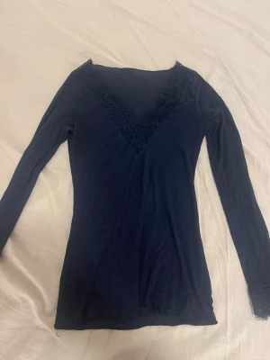 Svart långärmad topp med spets - Snygg svart långärmad topp med djup v-ringning dekorerad med spetsdetaljer från intimissimi, i storlek S. Tunn och mjuk i materialet, perfekt att styla till olika outfits. Enkel men elegant design som ger en chic vibe.