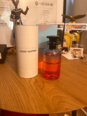 Louis Vuitton California Dream parfym - Louis Vuitton California Dream parfym i en snygg glasflaska med rosa-orange toning och svart spraymunstycke. Flaskan har tydlig logga och kommer med originalförpackning och elegant vit cylinderask. Perfekt för dig som gillar exklusiva dofter.