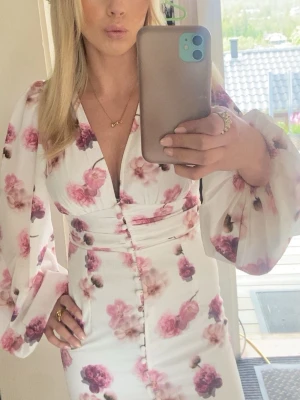 Adoore liknande klänning  - Supersnygg lång vit klänning med rosa blommönster och djup v-ringning. Klänningen har puffiga långa ärmar, markerad midja och knappar framtill hela vägen ner🌸🌸💕💕🌺