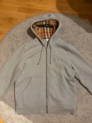 Burberry Full Zip Hoodie – Grå – Strl XL - Säljer en Burberry full zip hoodie i grått, storlek XL. Tröjan är nästan i nyskick och sparsamt använd. 	•	Nypris: 760 € (ca 8 100 kr) 	•	Köpt från Mytheresa 	•	100 % äkta – kontoutdrag/kvitto finns  Det finns många kopior ute av denna modell, men jag garanterar att denna är äkta. Därför är detta ett riktigt bra pris för en original Burberry-hoodie.  Hör av dig vid frågor eller om du vill ha fler bilder. Seriösa köpare prioriteras!