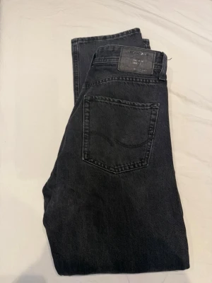 Svarta jeans från Jack and Jones  - Snygga svarta jeans från Jack and Jones  med klassisk femficksdesign och svart patch bak i midjan. Jeansen har raka ben och är tillverkade i mjuk bomullsdenim. Perfekta för en clean och stilren look.