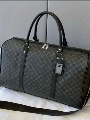 Svart mönstrad resväska  - Snygg svart resväska med klassiskt monogrammönster och detaljer i svart skinn. Väskan har dubbla handtag, avtagbar axelrem och dragkedja upptill. Perfekt för weekendresor och har en stilren, modern look.