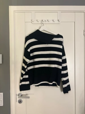 Svartvit randig stickad tröja - Snygg stickad tröja med breda svarta och vita ränder. Tröjan har en avslappnad passform, långa ärmar och en bred krage. Perfekt för en trendig och bekväm look. Materialet är mjukt och ribbstickat.