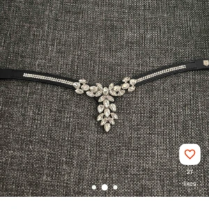 Svart pannband med strass och kristaller - Ett svart pannband dekorerat med gnistrande strass och stora kristaller i silverfärg. Pannbandet har en V-formad design med bladformade stenar i mitten och mindre stenar längs sidorna. Perfekt accessoar för hästutrustning eller show. Två kristaller e borttagna då dom va ivägen men är inget som syns. Bilder från min lofta profil.