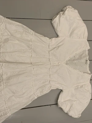 Vit sommrig klänning från Cubus  - Söt vit sommar klänning med puffärmar och v-ringning. Klänningen har broderade detaljer och en luftig, volangig kjol. Perfekt för sommarens alla tillfällen och ger en romantisk vibe. Tillverkad i bomull för en skön och sval känsla.